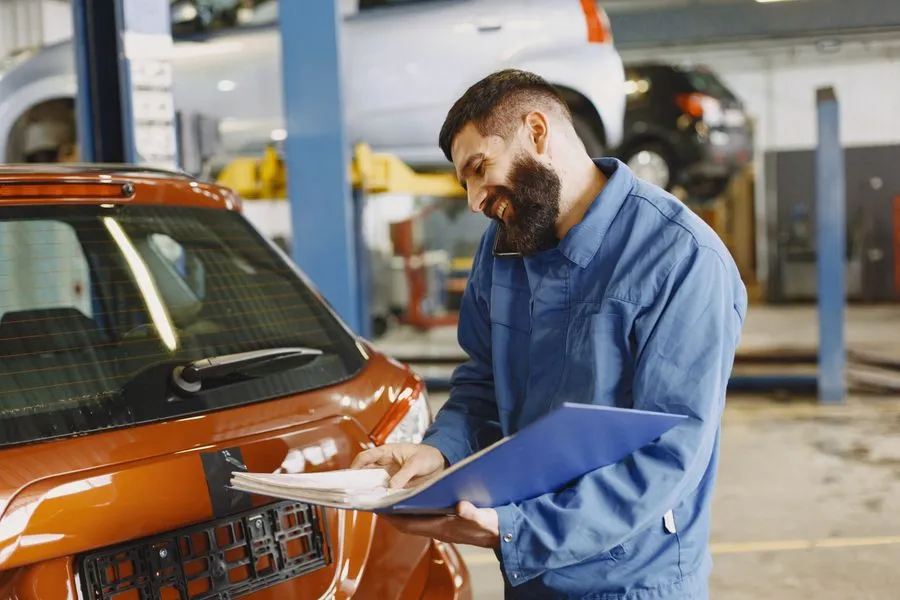 Mechanic reading a clipboard beside a car